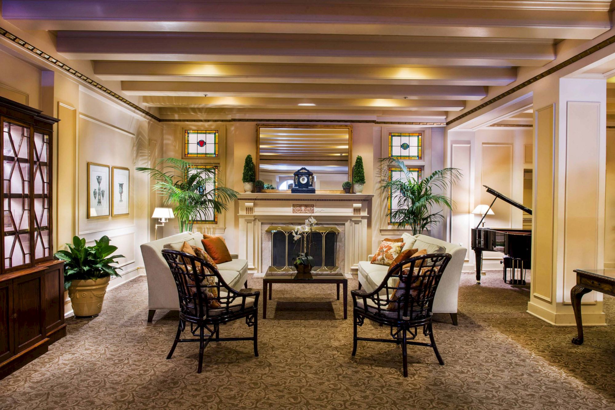 A cozy hotel lobby with a central fireplace, plush seating, potted plants, warm lighting, and a grand piano in a classic, elegant setup.