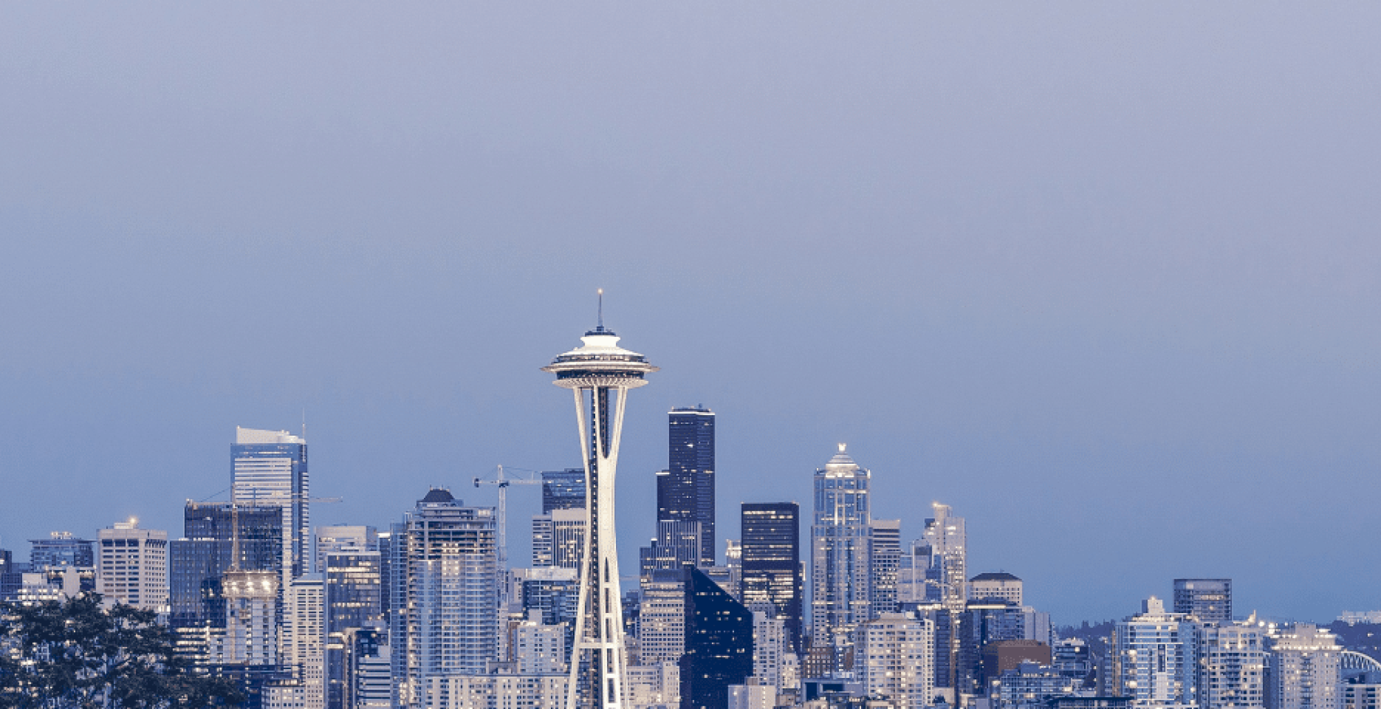 Seattle skyline at dusk with the Space Needle rising above many tall buildings, soft blue sky, calm urban glow. ending sentence.