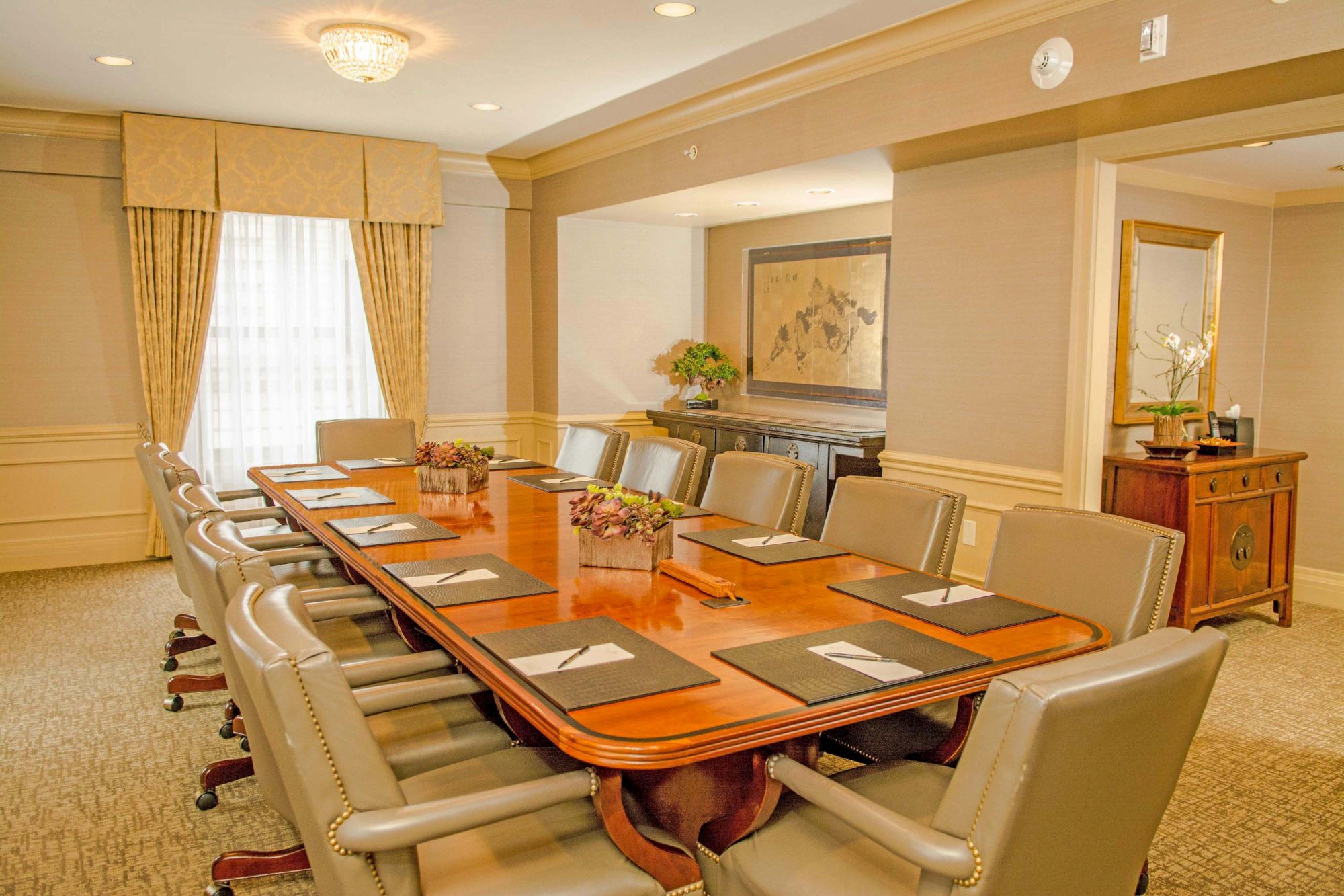 A formal conference room with a long wooden table, tan leather chairs, place settings, and soft beige walls; a serene, executive ambiance.