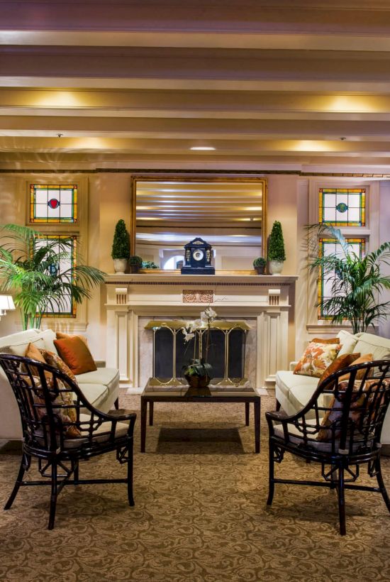A classy hotel lobby with a central fireplace, comfortable seating, potted plants, warm lighting, and a grand piano in the corner, inviting and elegant.