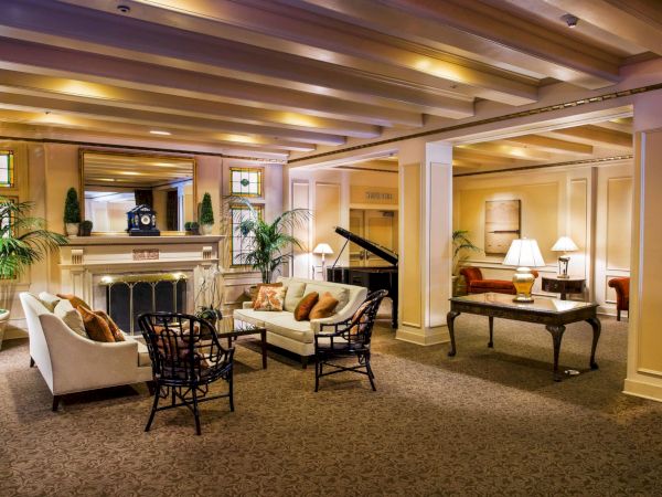 A luxurious hotel lobby with a grand piano, comfortable seating, warm lighting, plants, and a fireplace, creating an elegant, inviting space.