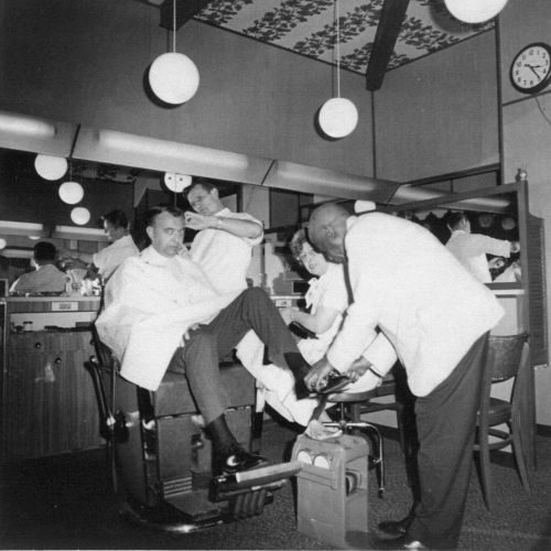 A vintage black-and-white scene of people socializing in a cozy, retro dining or bar setting, seated at tables and chatting.
