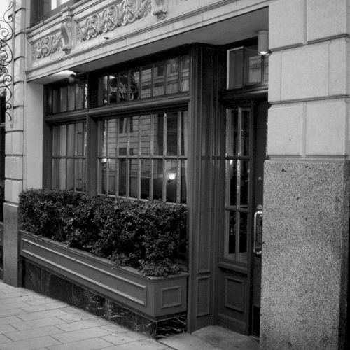 A black-and-white street storefront with a large display window and pedestrians passing by. Short, 140 characters, ending with a period.