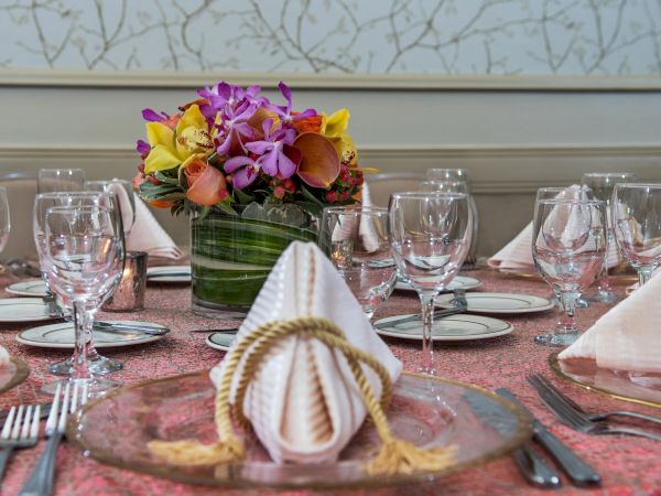 A formal dining table set with folded napkins, glassware, and a vibrant floral centerpiece in the middle, ready for guests.
