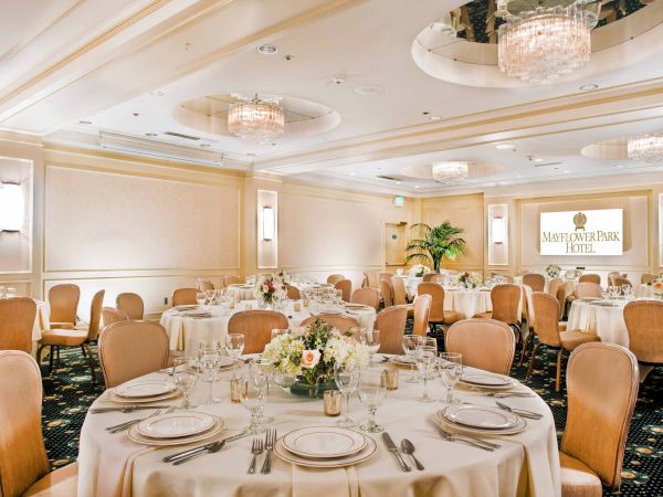 A formal banquet hall set for a classy event with round tables, white linens, elegant chairs, and chandeliers, likely a wedding or gala.