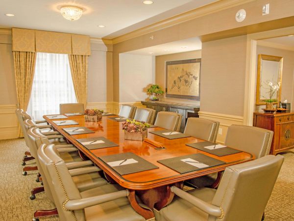A formal conference room with a long wooden table, beige chairs, place settings, and soft warm lighting in an elegant, professional space.