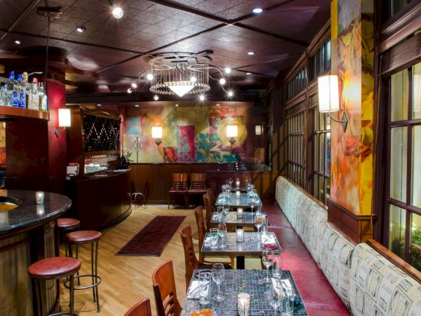 A stylish, dimly lit restaurant bar with a long dining table setup, colorful murals, and modern art accents along the walls.