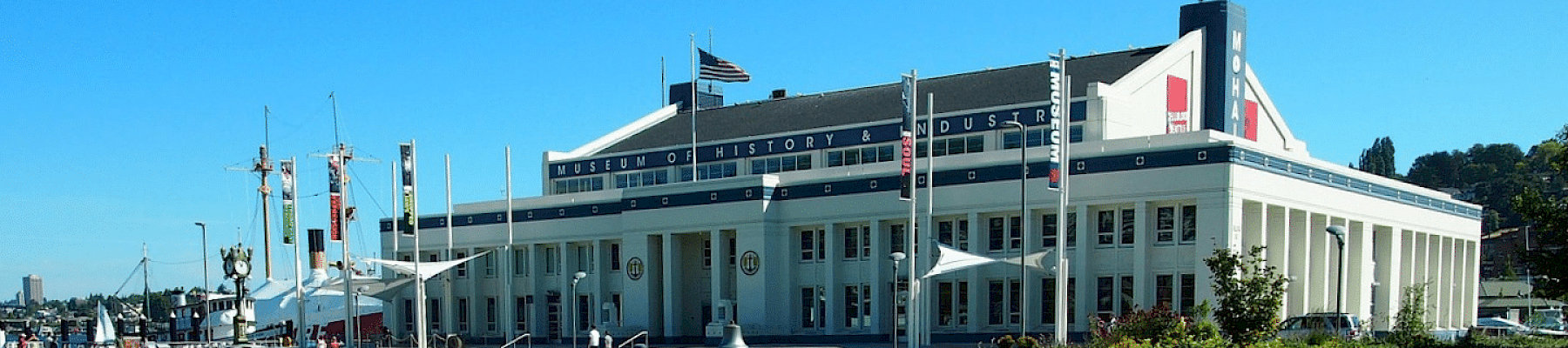 A neoclassical museum building with columns, flags, and a curved walkway; a bright day with a blue sky and people around the entrance.