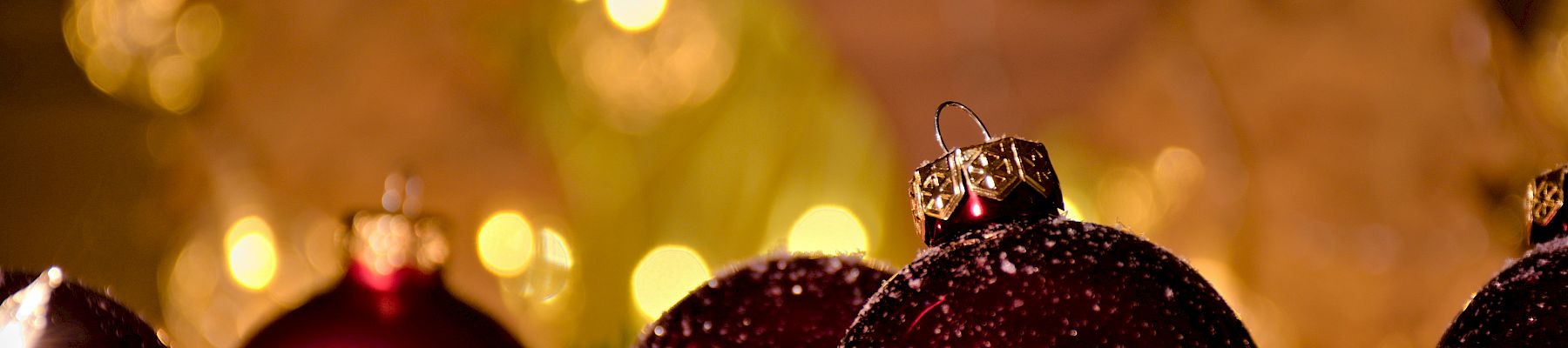Shiny red Christmas ornaments among pine branches and snow, with warm glowing lights in the blurred background, festive and cozy.